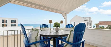 Un área de estar al aire libre cubierta con una mesa y sillas, con vista a la playa.