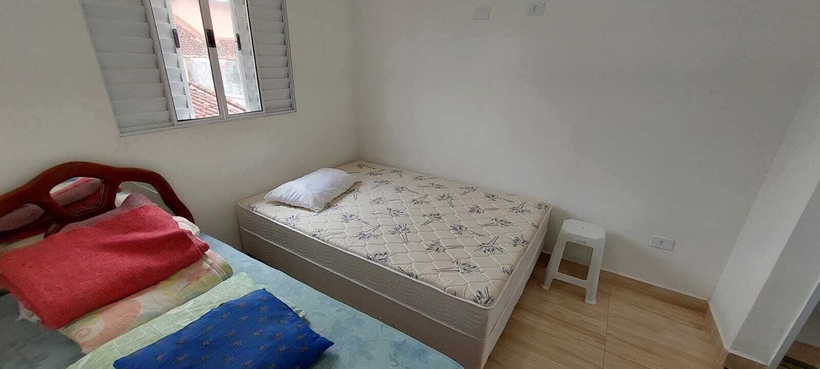 Une petite chambre avec un lit simple, une tête de lit en bois, un petit tabouret blanc et une fenêtre avec des stores.