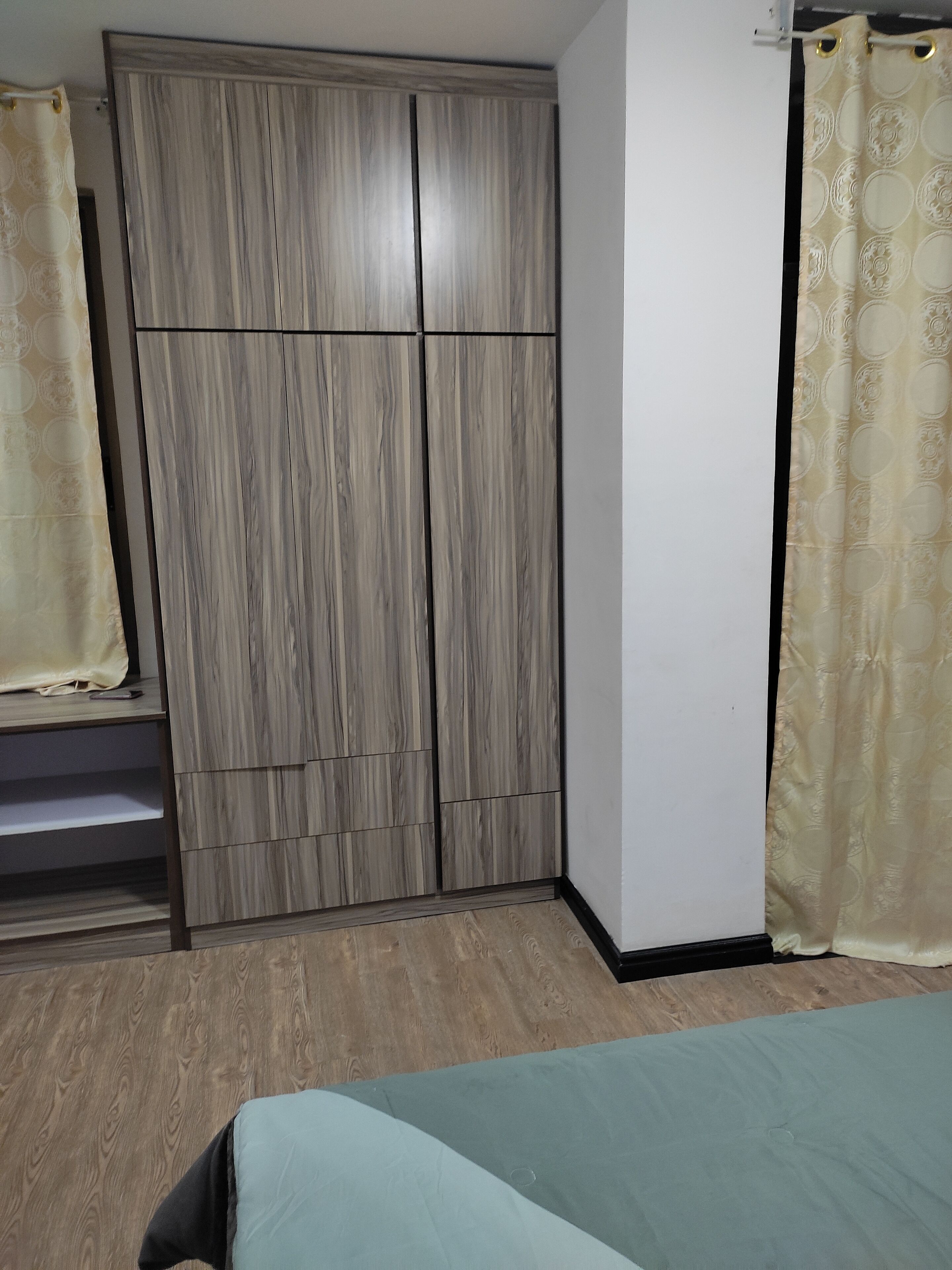 A bedroom with a wardrobe, a bed, and curtains.