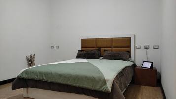 Un dormitorio ordenado con cama, mesitas de noche y estación de carga en la pared.