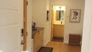 Un couloir au plancher de bois menant à une cuisine équipée d’un évier et de placards.