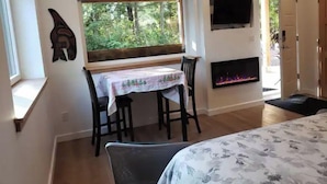 Une pièce chaleureuse comprenant une table à manger, des chaises, une cheminée, un téléviseur et une fenêtre donnant sur un paysage verdoyant.