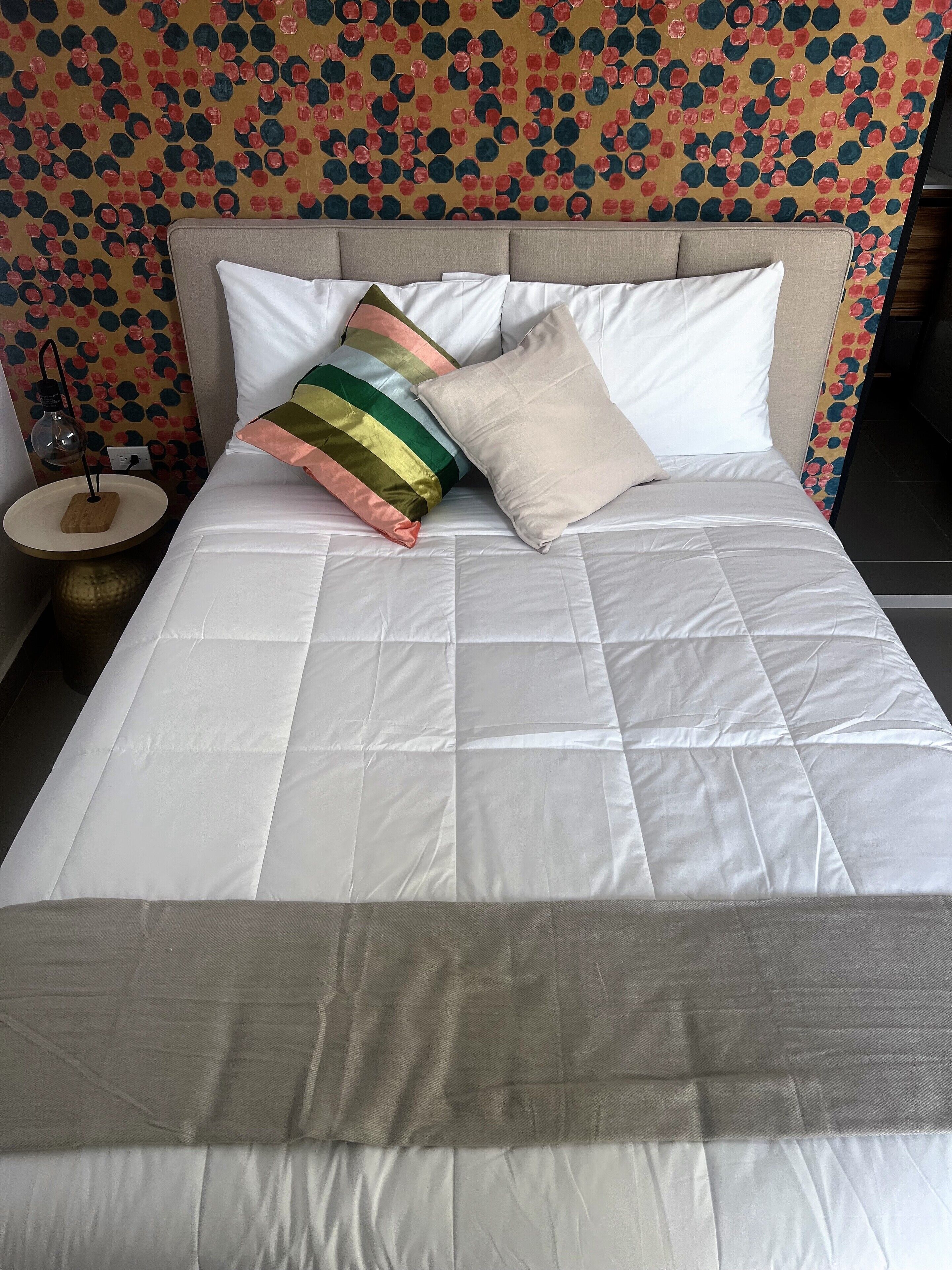 A neatly made bed with white bedding and a variety of pillows, including a striped one.