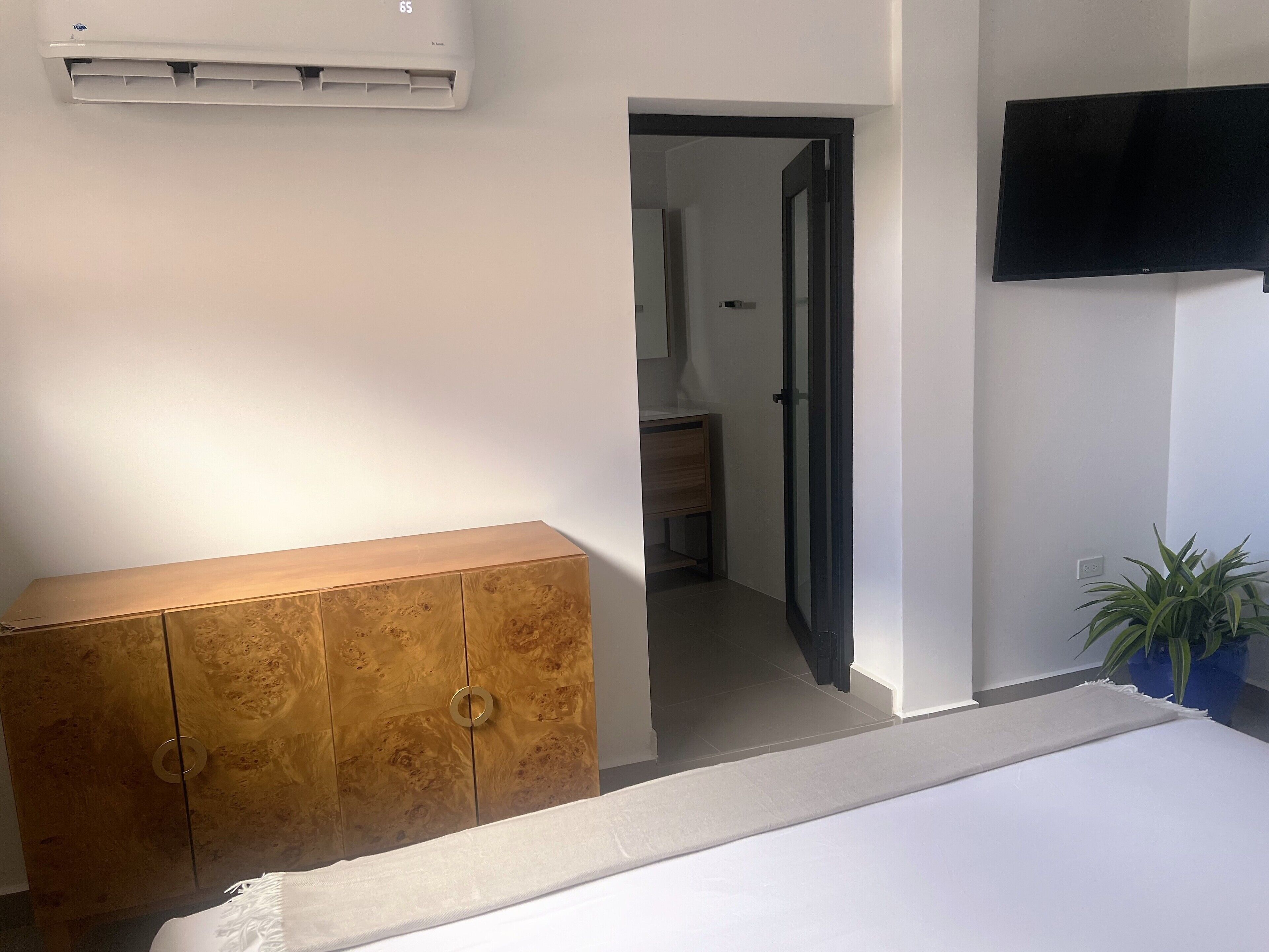 A bedroom with a wooden wardrobe, a bed, a TV mounted on the wall, and a potted plant.