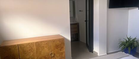 A bedroom with a wooden wardrobe, a bed, a TV mounted on the wall, and a potted plant.