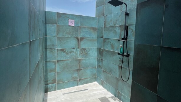 Un baño moderno con baldosas teal grandes, una zona de ducha y un suelo de tonos claros.