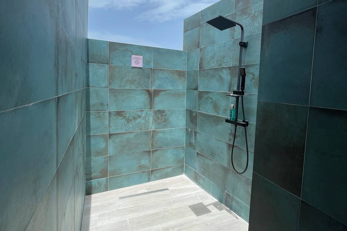 A modern bathroom with large teal tiles, a shower area, and a light-colored floor.