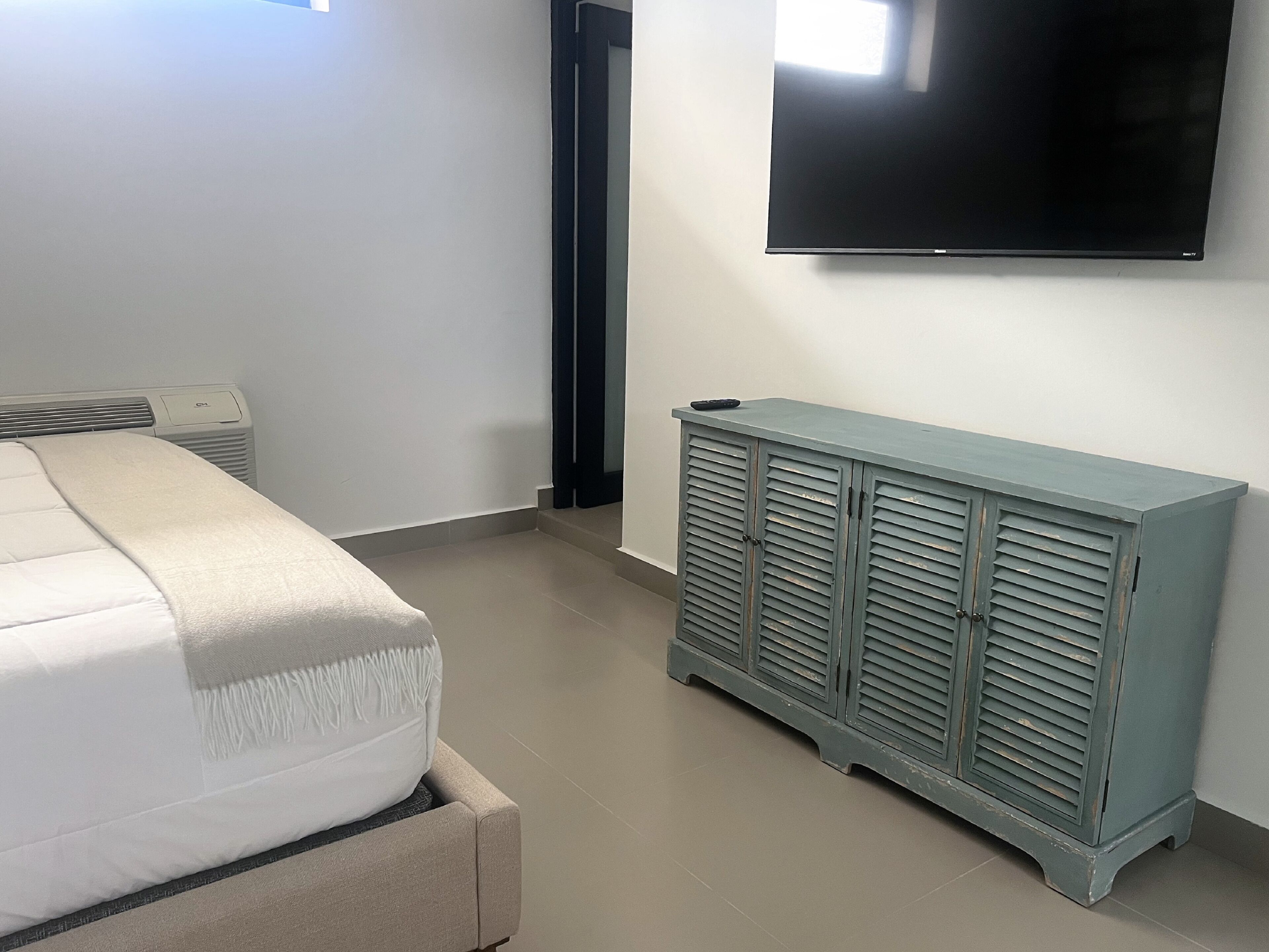 A bedroom with a bed, a TV mounted on the wall, a radiator, and a cabinet.
