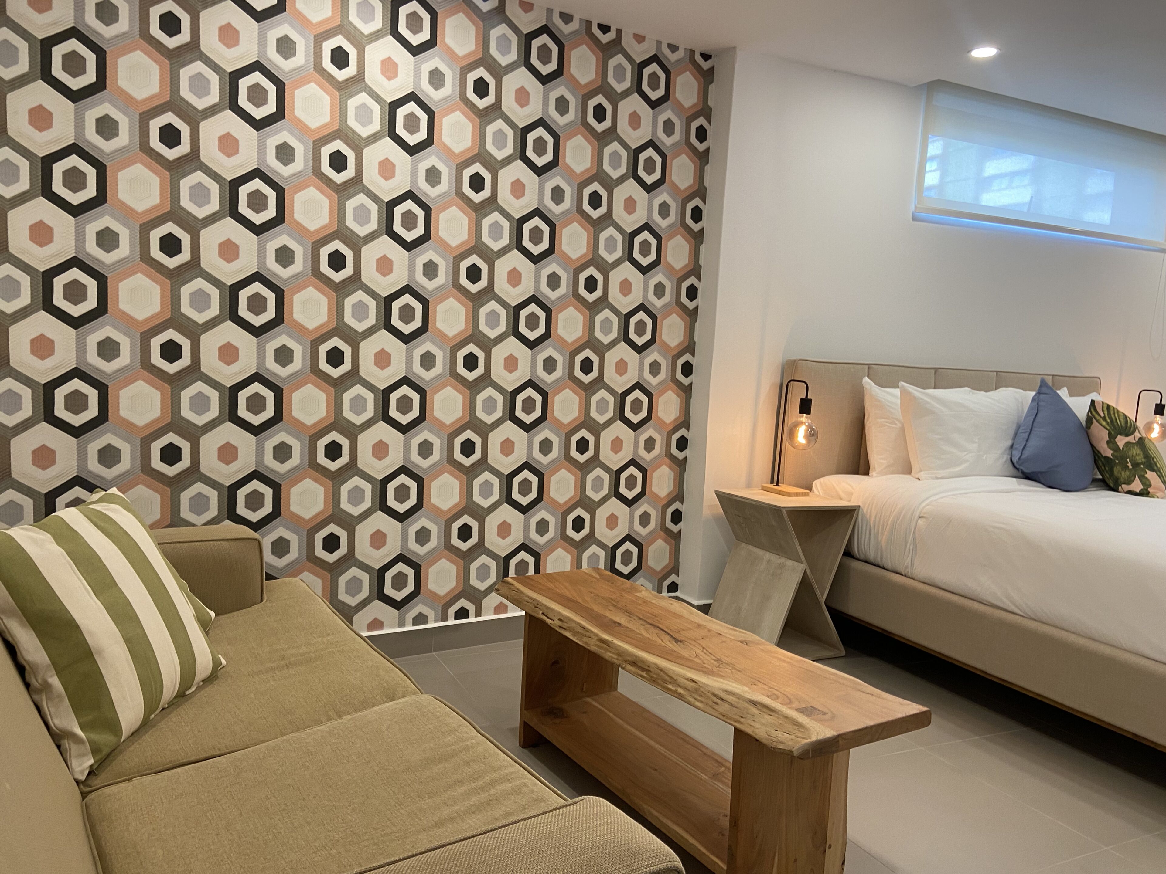 A modern bedroom with a geometric-patterned wall, a bed with white bedding, a wooden nightstand, and a striped pillow.
