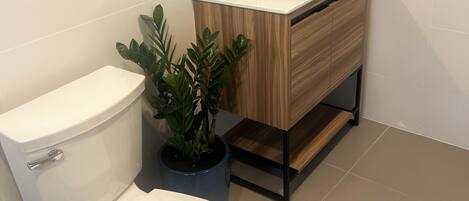 A modern bathroom with a white toilet, a sink with a wooden vanity, and a mirror above the mirror cabinet.