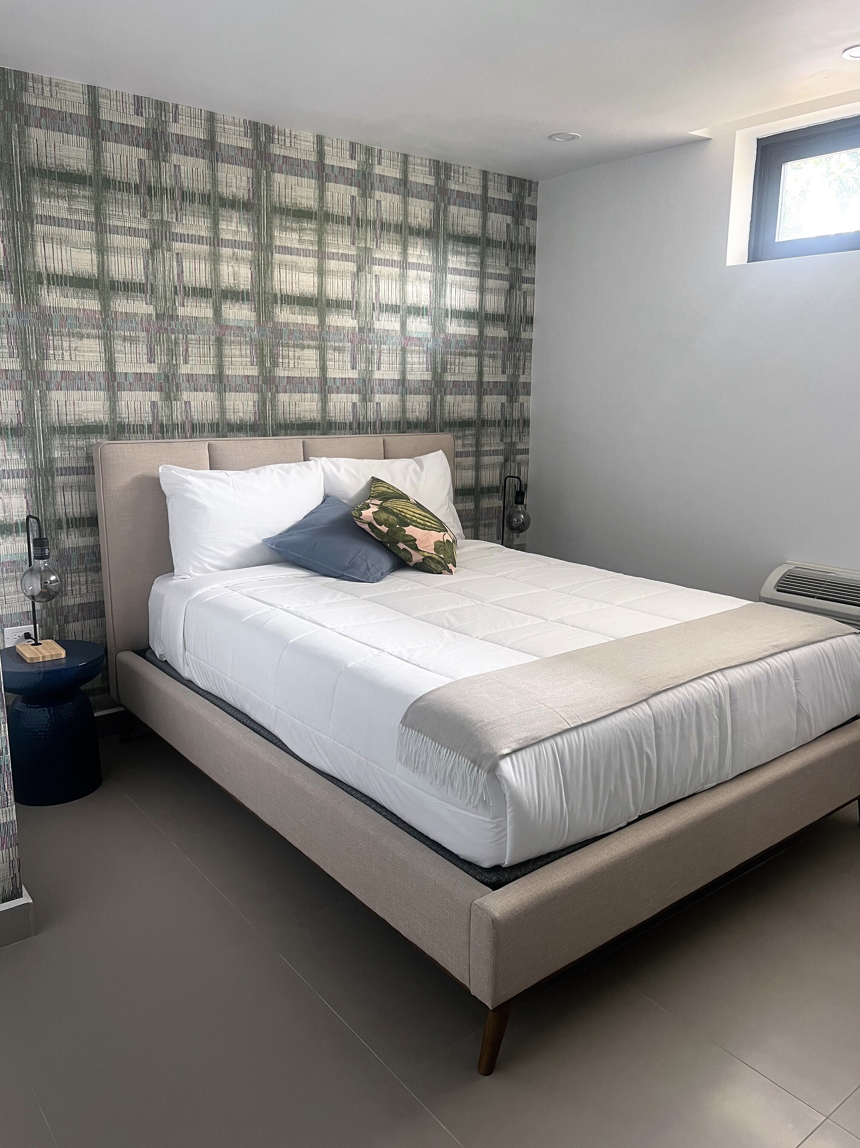A modern bedroom with a large bed, a bedside table, and a window.