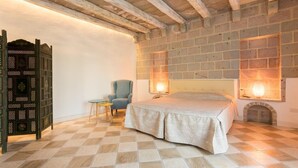 Une chambre avec un sol à carreaux, un lit, une chaise, une petite table et un paravent décoratif.