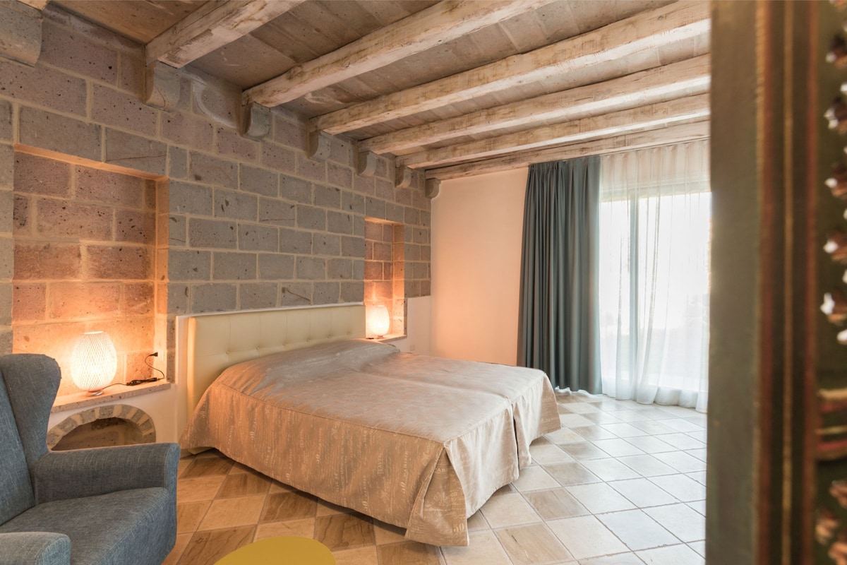 Ein Schlafzimmer mit Backsteinwand, einem Bett, einem Stuhl und einem Fenster mit Vorhängen.