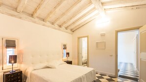 Une chambre avec un sol à carreaux, un lit avec une literie blanche, une table de chevet avec une lampe et un plafond en bois.