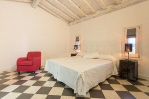 A bedroom with a checkered floor, a bed with white bedding, a red chair, and a nightstand with a lamp. - La Petite Maison (Tresnuraghes)