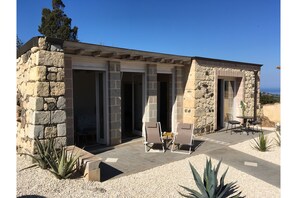 A stone building with a patio area featuring outdoor seating and a view of the sea. - La Petite Maison (Tresnuraghes)