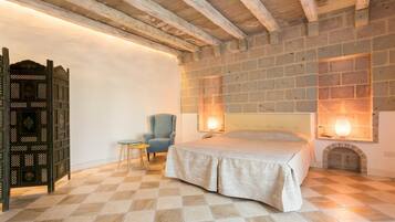 Un dormitorio con piso de cuadros, una cama, una silla, una mesita y un biombo decorativo.