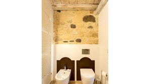 Une salle de bain avec un mur en pierre, un bidet, des toilettes et un porte-serviettes.