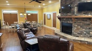 A living room with a stone fireplace, leather sofas, and a dining area with chairs and tables.