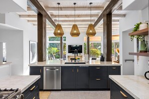 Une cuisine moderne dotée d’un îlot central, d’appareils électroménagers en acier inoxydable et de luminaires suspendus.