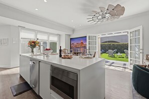 A modern kitchen with a central island, built-in appliances, and a view of a landscaped garden through an open door.