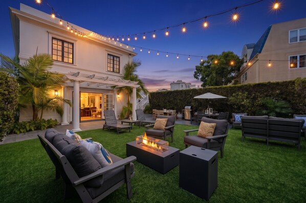 A well-lit outdoor patio area with a fire feature, seating, and string lights.