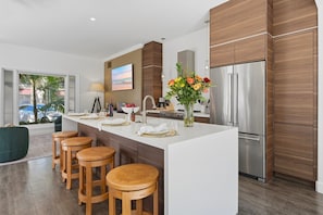 A modern kitchen with a central island, bar stools, stainless steel appliances, and a large window with a view.