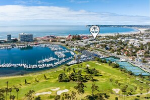 A marina with multiple boats docked, a golf course, and residential buildings in the background. - Walk to Beaches, Dining & Everything Coronado Has to Offer | Coronado Crown Vi (Coronado)