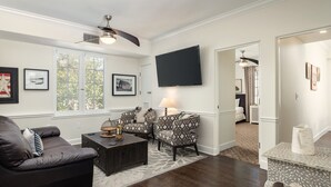 Un salon doté d’un parquet en bois foncé, d’un canapé en cuir noir, de fauteuils à motifs, d’une table basse et d’un téléviseur à écran plat fixé au mur.