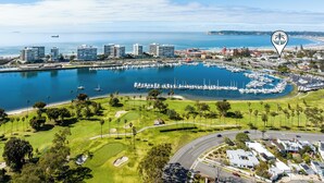 Vue aérienne d’une marina avec des bateaux, un terrain de golf et des immeubles résidentiels.