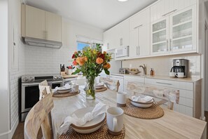 A modern kitchen with white cabinetry, a central island with a vase of flowers, and a coffee maker on the countertop.