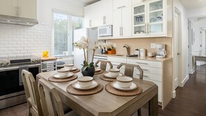 Une cuisine moderne avec des meubles blancs, un four à micro-ondes encastré et un coin repas agrémenté d’assiettes et de bols blancs.