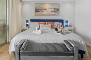 Uma cama bem arrumada com um edredom branco, duas almofadas, um tabuleiro com uma garrafa, copos e um objeto decorativo.