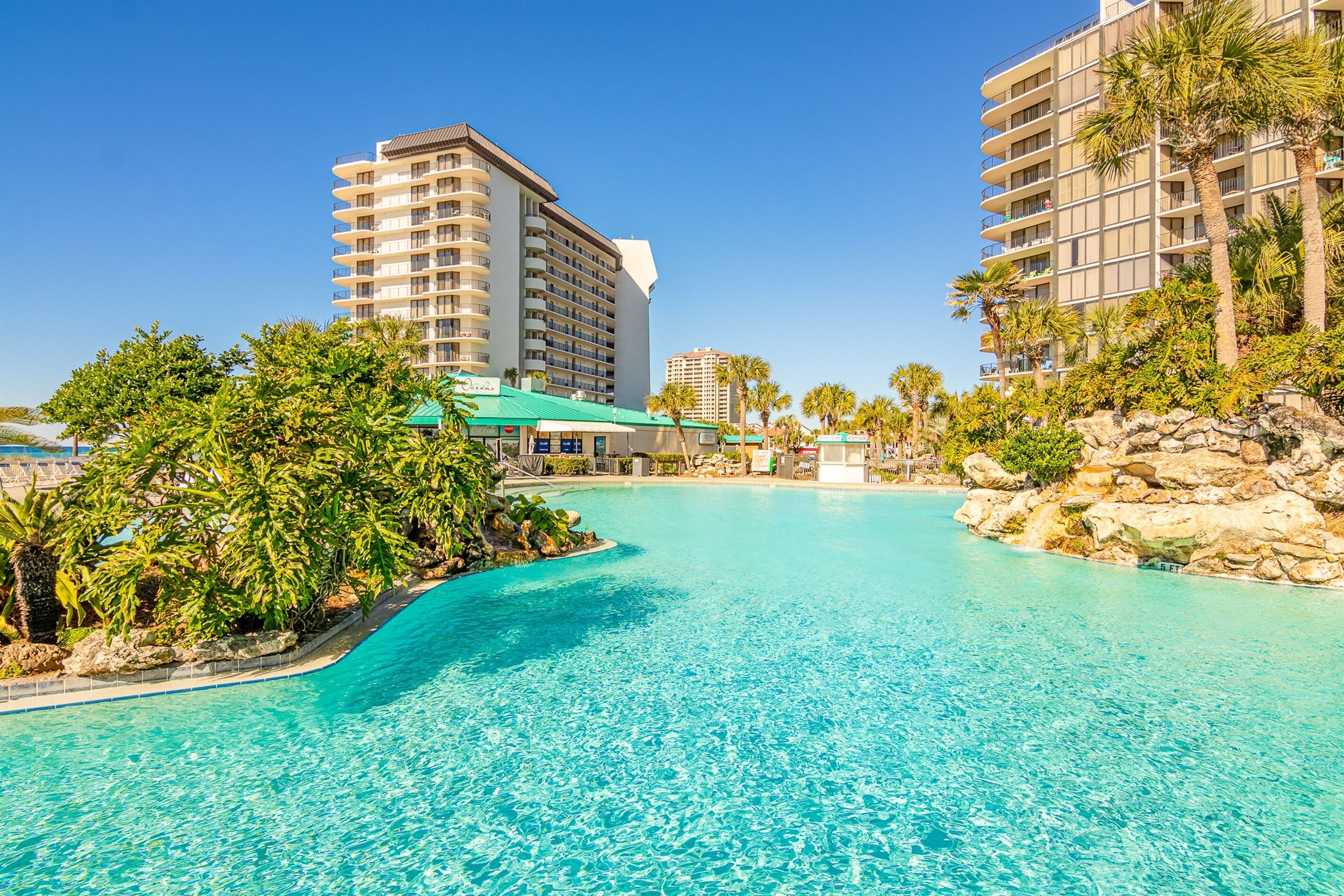 A hotel with a large pool, surrounded by palm trees and a rocky landscape.