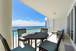 A balcony with a round wooden table and chairs, overlooking a beach.
