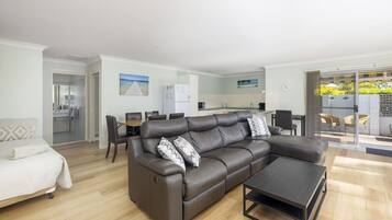 A modern living room with a leather sofa, a dining table, and a kitchen in the background.