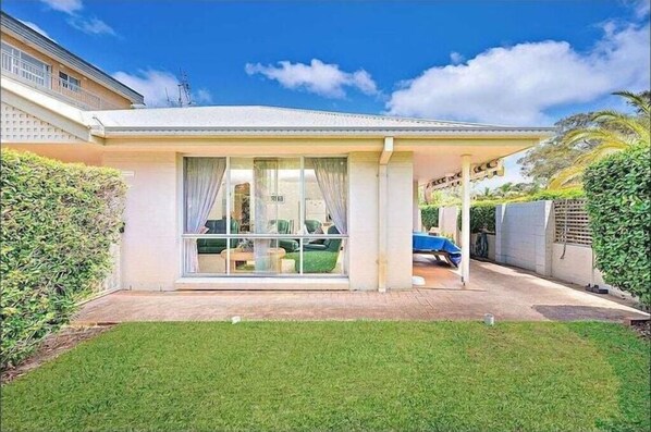Eingeschossiges Haus mit überdachter Terrasse, großen Schiebeglastüren und einem gepflegten Rasen.