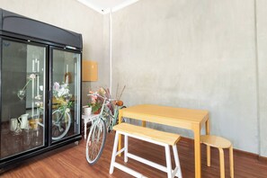 Une pièce avec une table et un banc en bois, un vélo et un réfrigérateur à portes vitrées.