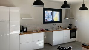 Cocina moderna con armarios blancos, encimera de madera y lámparas colgantes negras.