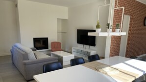 Una sala de estar moderna con un sofá gris, una mesa de centro blanca, un televisor de pantalla plana y una pared de ladrillo.