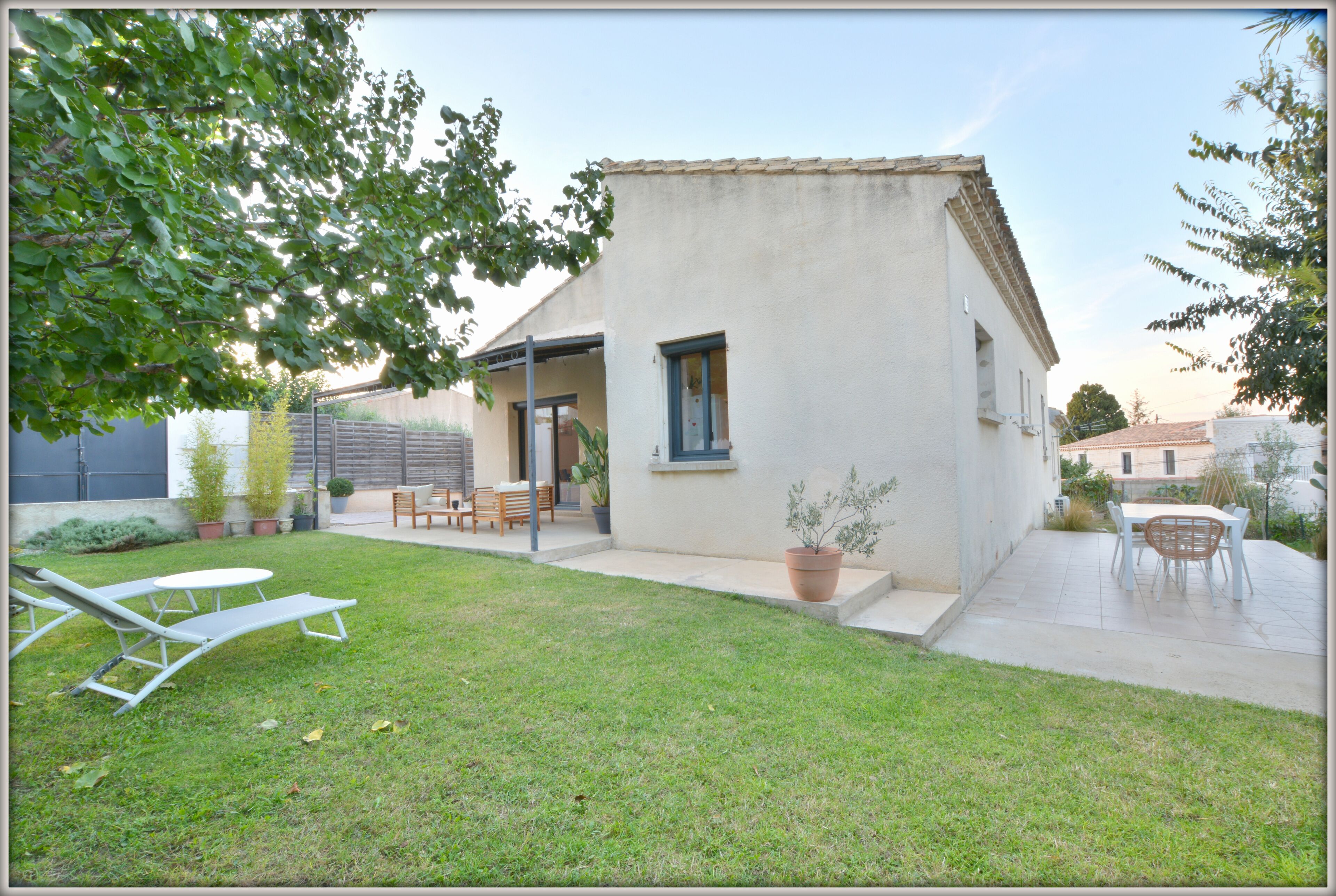 Une petite maison avec un patio, une pelouse et du mobilier d’extérieur.