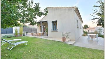 Une petite maison avec un patio, une pelouse et du mobilier d’extérieur.