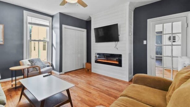 Ein modernes Wohnzimmer mit Kamin, Deckenventilator und flachbildfernseher an der Wand.