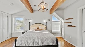 Ein Schlafzimmer mit einem Bett, Holzbalken, einer Hängeleuchte und Fenstern.