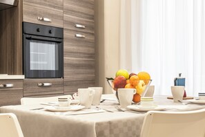 A modern kitchen with a built-in oven and a dining area with a table set for breakfast. - Casina Rossa (Naples)