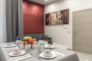 Een eethoek met een tafel voor vier personen, een fruitmand en een schilderij aan de muur.