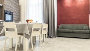 A modern dining area with a table set for four, a sofa, and a kitchen with a built-in oven. - Casina Rossa (Naples)