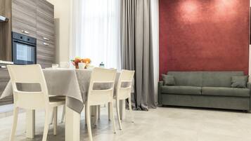 Un espace repas moderne avec une table dressée pour quatre personnes, un canapé et une cuisine équipée d’un four encastré.