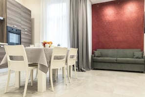 Een moderne eetruimte met een tafel voor vier personen, een bank en een keuken met een ingebouwde oven.