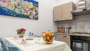 Una cucina moderna con elettrodomestici in acciaio inossidabile, un'area pranzo con tovaglia bianca e un quadro che raffigura un vivace paesino costiero.